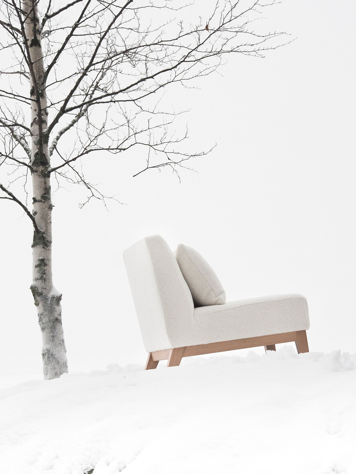 Nagu-nojatuoli valkoisella kankaalla verhoiltuna sivusta kuvattuna. Jalat ja kehikko tammea.