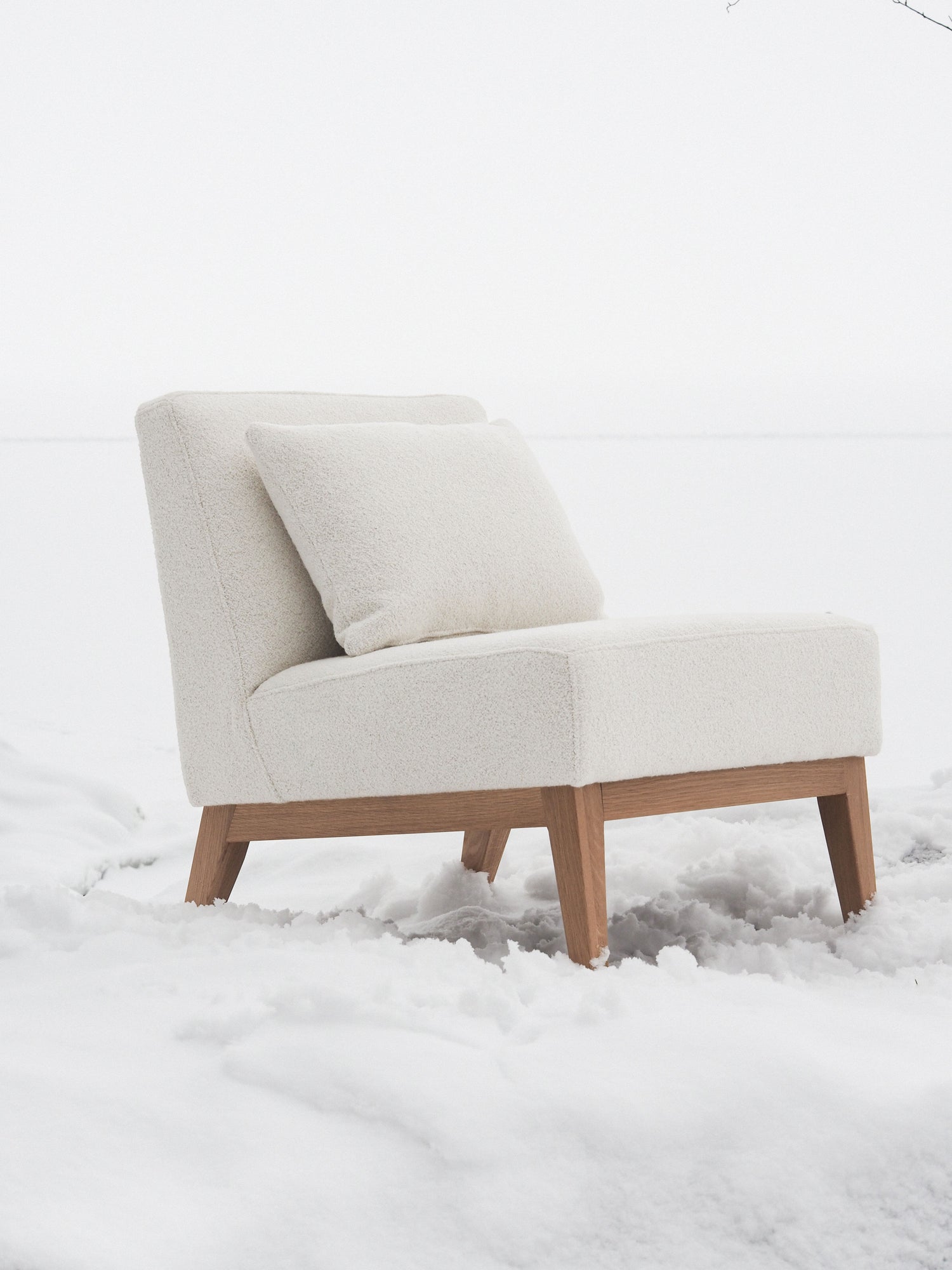 Nagu-nojatuoli valkoisella kankaalla verhoiltuna. Jalat ja kehikko tammea. Tuolilla valkoinen tyyny.