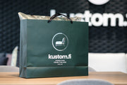 Vihreä paperikassi, jossa Kustom-logo ja teksti "Kustom.fi furniture from Finland since 1970".